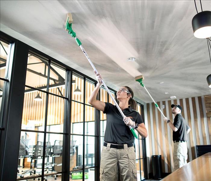 SERVPRO production technician woman cleaning a ceiling with a sponge on a pole